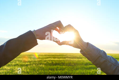 Couple romantique dans l'amour des gestes un coeur avec les doigts sur le coucher du soleil Banque D'Images