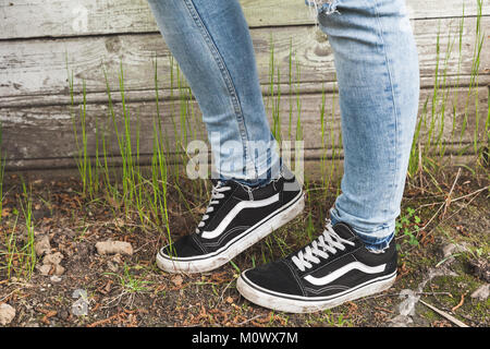 Adolescent pieds de blue-jeans et baskets noires se tiennent près de vieux grungy mur en bois en milieu rural Banque D'Images