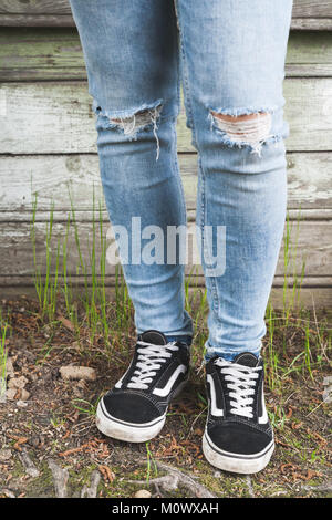 Adolescent pieds de blue-jeans et baskets noires se tiennent près de vieux mur en bois rural grungy, photo verticale Banque D'Images