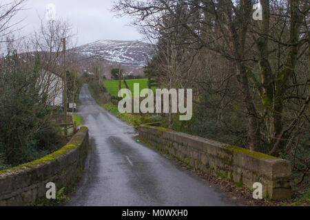 Vue sur un petit pont de pierre avec un pic enneigées d'une des montagnes de Mourne dans l'arrière-plan sur un après-midi de l'hiver terne Banque D'Images