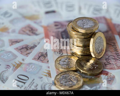 Une pile de nouvelles pièces de livres britanniques placées sur un cercle de nouveaux billets de dix livres sterling avec une pièce sur son bord et trois autres couchées à plat Banque D'Images