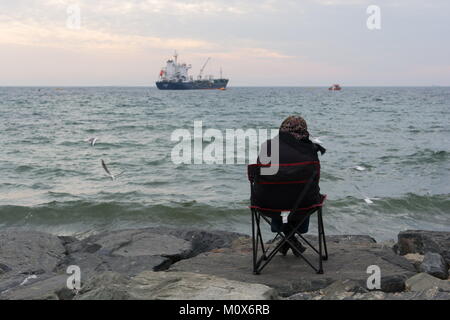 Vieille Femme est assise au bord de la plage. De là, regardant les bateaux et les oiseaux.prévenant Banque D'Images