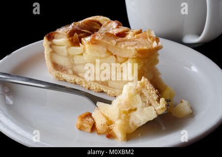 Une tranche de tarte aux pommes avec pie sur fourche sur une plaque en céramique blanche à côté de la fourchette. Fond noir. Banque D'Images