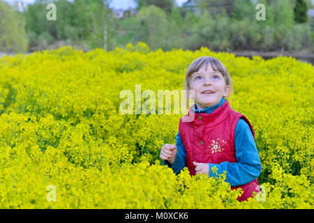Sourire mignon petite fille sur la prairie jaune au printemps. Domaine de Barbarea vulgaris, également appelé comme bittercress, herb barbara, rocketcress Banque D'Images