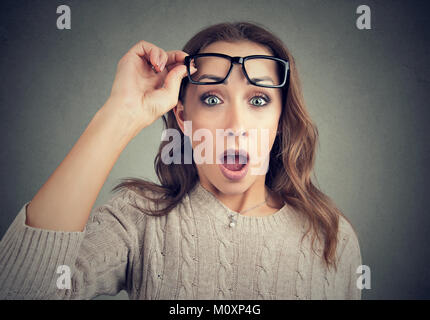 Young casual woman taking off lunettes et looking at camera avec choc. Banque D'Images