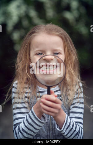 En tirant l'enfant stupide visage derrière une loupe Banque D'Images