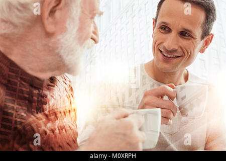 Genre Homme attentif en regardant son vieux père tout en buvant du café Banque D'Images