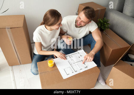 Couple discussing plan de maison sitting on floor with moving boxes Banque D'Images