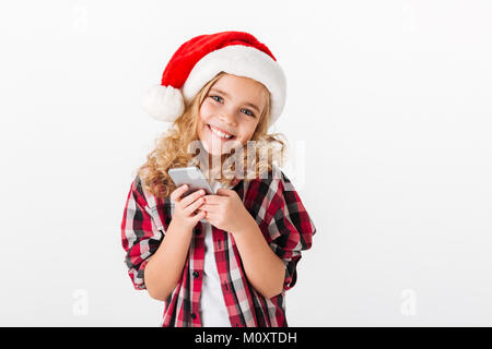 Portrait d'une jolie petite fille vêtue de christmas hat holding mobile phone isolé sur fond blanc Banque D'Images