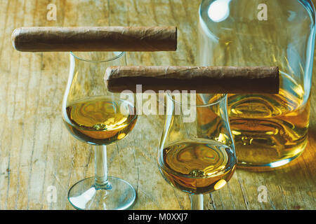 Photo en gros plan de la vie toujours avec deux cigare, une bouteille d'alcool et un verre de whisky sur une vieille table en bois, avec un arrière-plan flou Banque D'Images