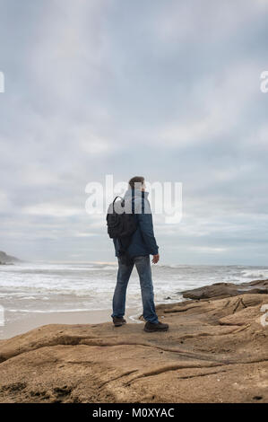 Homme portant un sac à dos sur les rochers à la recherche permanent sur l'océan. Banque D'Images