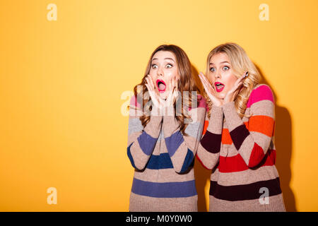 Portrait de deux jeunes filles vêtues de pulls choqué à loin à l'espace de copie plus isolé sur fond jaune Banque D'Images