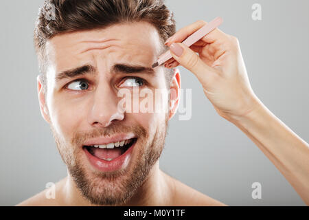 Main femme peur plumer des sourcils pour hommes avec des brucelles isolées sur fond gris Banque D'Images