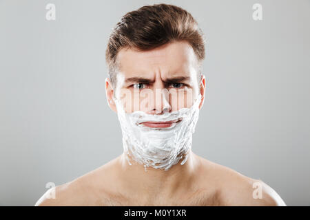 Portrait d'un homme drôle avec mousse à raser sur son visage sur fond gris isolé Banque D'Images
