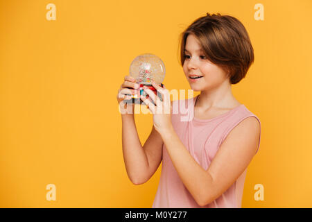 Handsome smiling girl in dress holding et à la neige à globe isolated sur jaune Banque D'Images