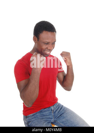 Un beau jeune homme afro-américain assis dans un chandail rouge avec ses poings et souriant de la victoire et le succès, isolé sur fond blanc Banque D'Images