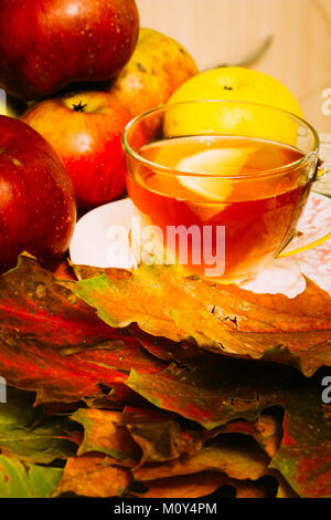 Thé au citron dans une tasse en verre parmi l'automne feuilles d'érable et pommes rouges bien mûrs. Composition Banque D'Images