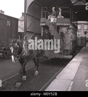 années 1950, historique, à une station de tramway, à côté de la plate-forme, un homme debout sur un tramway tiré par des chevaux près de l'escalier et deux enfants se promenant sur le pont supérieur. Ce tram tiré par des chevaux à Fintona, dans le comté de Tryone, en Irlande du Nord, était le dernier en Irlande à rester en service, mais fermé en 1957 après 104 ans, ainsi que les deux gares ferroviaires dans le village, Fintona et Fintona Junction, qui est relié par le tramway. Banque D'Images