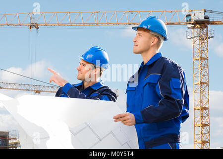 Deux jeunes hommes à la recherche d'architecte dans Blueprints At Construction Site Banque D'Images