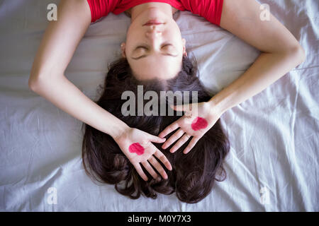 Attractive brunette jeune femme avec coeur dessin sur les mains dans le lit Banque D'Images