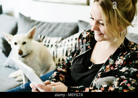 Jeune femme assise sur le canapé avec son chien et ressemble à un ordinateur tablette,Allemagne Banque D'Images