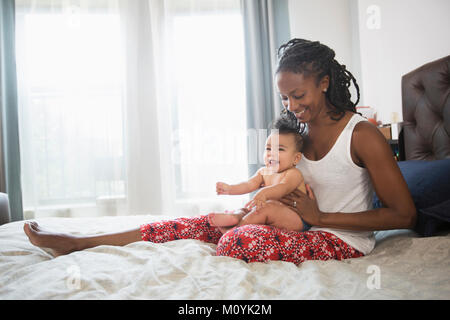 Mother sitting on bed holding baby daughter on lap Banque D'Images