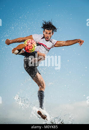 Pulvérisation d'eau sur man kicking soccer ball Banque D'Images