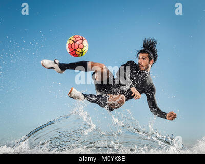 Pulvérisation d'eau sur man kicking soccer ball Banque D'Images