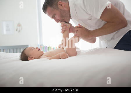 Père kissing feet of baby son on bed Banque D'Images