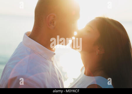 Caucasian couple kissing près de ocean at sunset Banque D'Images