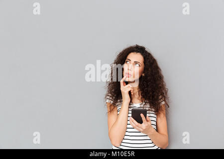 Photo de belle femme de toucher ses lèvres et à côté en pensant à quelque chose d'important ou d'essayer de se souvenir, plus d'arrière-plan gris Banque D'Images