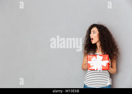 Portrait de heureux et franc avec les cheveux noirs bouclés holding red fort d'un emballage-cadeau, d'être excité et surpris copy space Banque D'Images