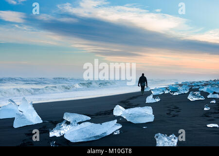 Un photographe masculin balades parmi les icebergs échoués le long de la plage au coucher du soleil, Jokulsarlon Islande Banque D'Images