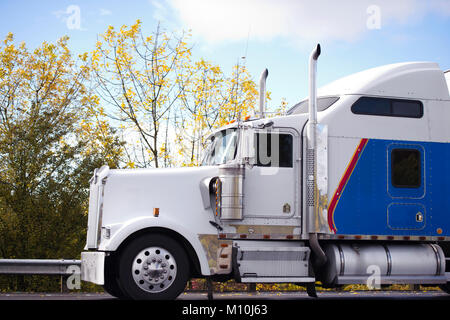 Profil de l'idole américain popular big rig blanc et bleu classique semi truck avec des tuyaux d'échappement et accessoires de chrome et un autre grand cab Banque D'Images