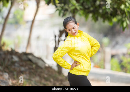 Un portrait d'une jeune femme asiatique en plein air l'exercice neon yellow jacket, blessé sa taille Banque D'Images