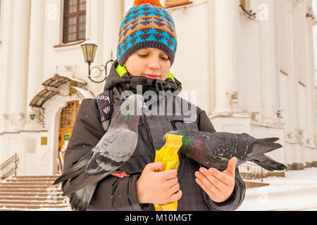 Le garçon nourrit les pigeons sur ses mains, debout sur la place en face de la cathédrale Banque D'Images