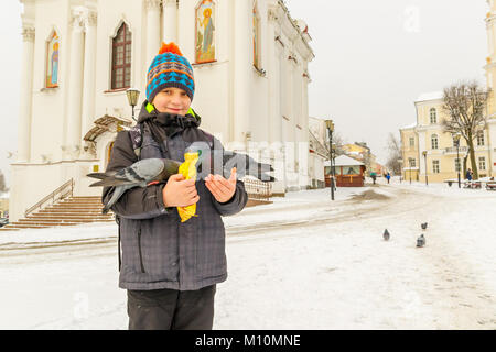 Le garçon nourrit les pigeons sur ses mains, debout sur la place en face de la cathédrale Banque D'Images