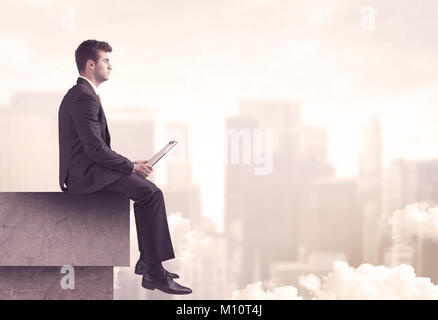 Une affaire sérieuse personne assise avec un ordinateur portable et tablette au bord d'un grand bâtiment, à plus nuageux concept city scape Banque D'Images