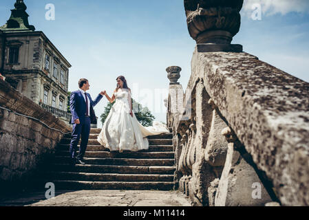 Portrait de mariage pleine longueur de l'adorable couple descendant le vieux château strais. Le marié est d'aider son amant avec la main. Banque D'Images