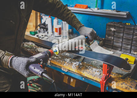 Un homme en vêtements de travail un réparateur à un atelier ski service ski une surface de glissement, polissage, Base de ski finale le polissage. Dans les mains d'une brosse électrique Banque D'Images