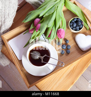 Un plateau avec thé et d'épices en forme de cœur et un bouquet de tulipes sur la chaise Banque D'Images