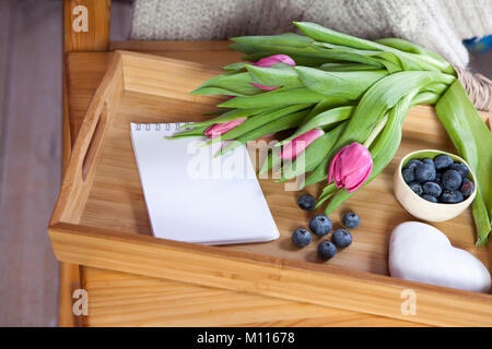 Un plateau avec thé et d'épices en forme de cœur et un bouquet de tulipes sur la chaise Banque D'Images