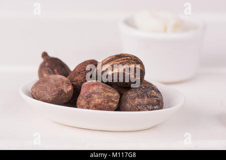 Noix de beurre de karité sur tableau blanc avec une tasse de beurre de karité, fermez-la. Banque D'Images