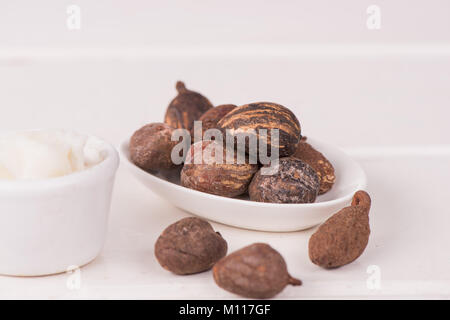 Noix de beurre de karité sur tableau blanc avec une tasse de beurre de karité, fermez-la. Banque D'Images