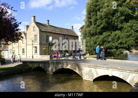 Bourton-on-the-water, Angleterre - 7 octobre 2010 : les visiteurs et les touristes de profiter du soleil d'automne dans 'la Venise du Cotswolds' comme Bourton-on-the-eau est parfois appelé. La première des cinq ponts de pierre a été construit en 1654. UK, Gloucestershire, Cotswolds, Bourton-on-the-l'eau. Les touristes profitant du soleil d'automne par la rivière. Banque D'Images