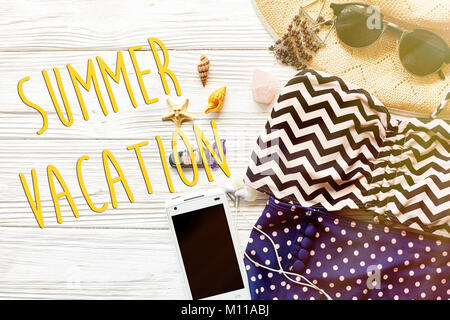 Vacances d'été concept texte télévision lay. maillot élégant de couleur, lunettes de soleil et chapeau coquillages et téléphone avec le casque sur fond de bois blanc, haut Banque D'Images