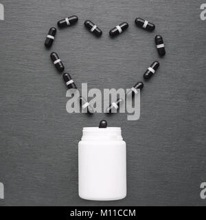 Capsules noires disposées en forme de coeur sont versées à partir de la bouteille blanche. Haut de la vue, télévision lay, copiez l'espace. Thème de la médecine, les soins de concept Banque D'Images