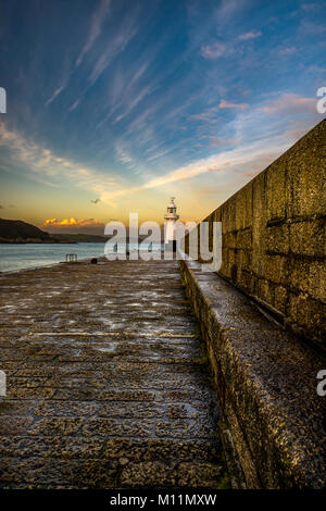 Mevagisseys mur du port et phare baigné dans l'heure d'or soleil comme dernière lumière se rapproche. Banque D'Images