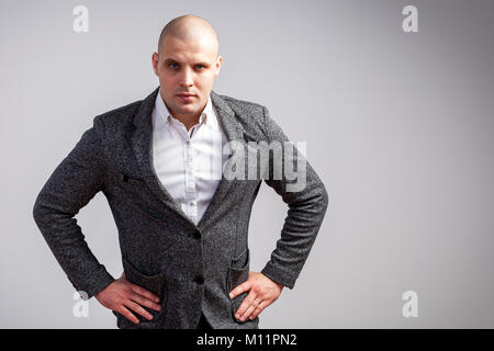 Jeune homme chauve en chemise blanche, costume gris regarde strictement caméra et détient les mains sur fond isolé sur blanc taille Banque D'Images