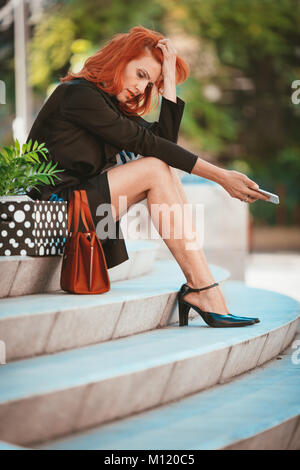 De graves pensive businesswoman sitting on stairs à côté d'une boîte pleine de ses effets personnels du bureau juste après elle s'est tiré. Banque D'Images